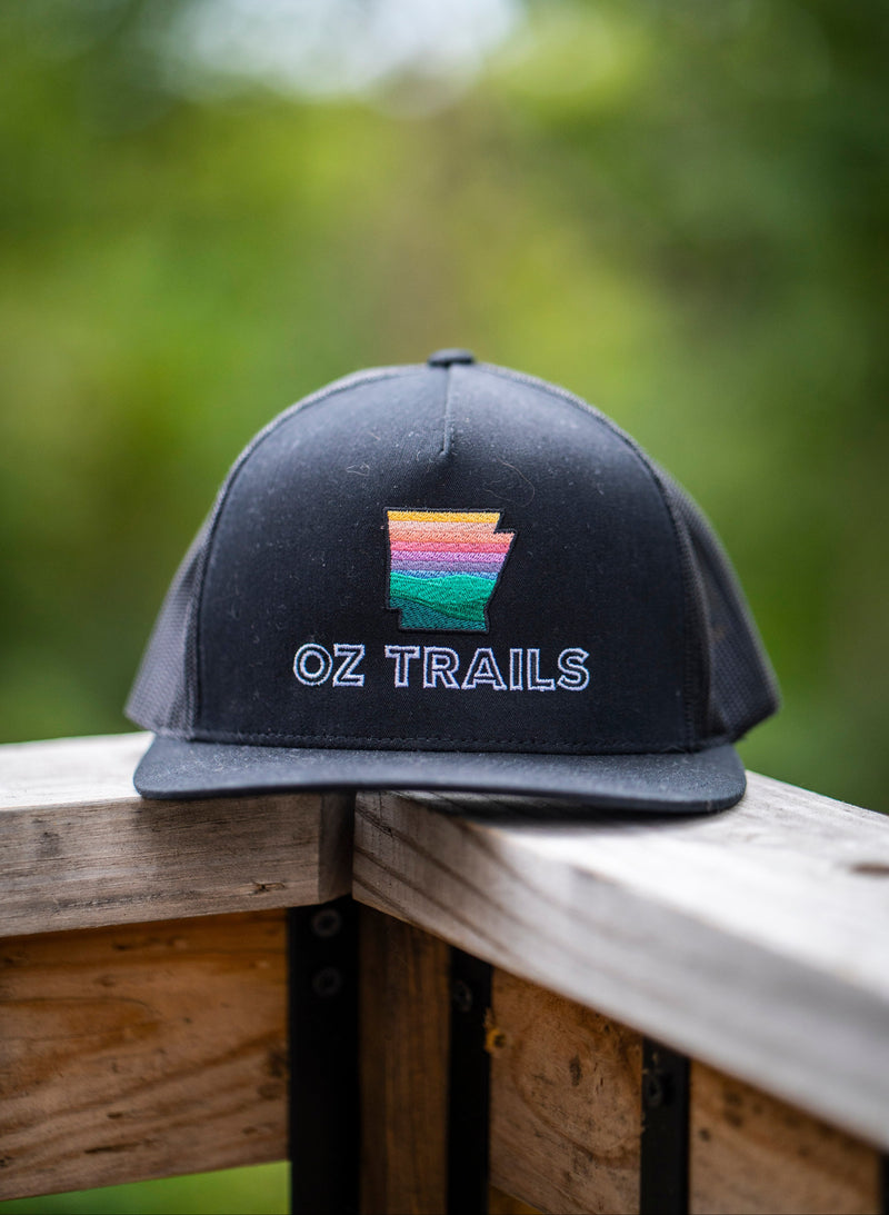 Black cap with 'OZ TRAILS' logo on a wooden surface with a blurred green background